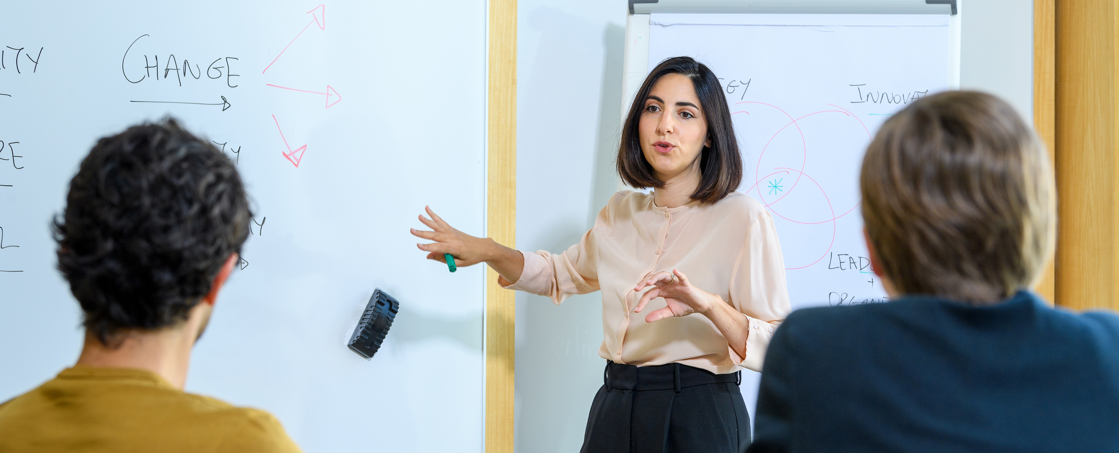 Female professor standing in front of white board teaching students 